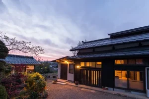 薪ストーブの煙突が映える古民家の夜の外観・農家住宅の空き家再生